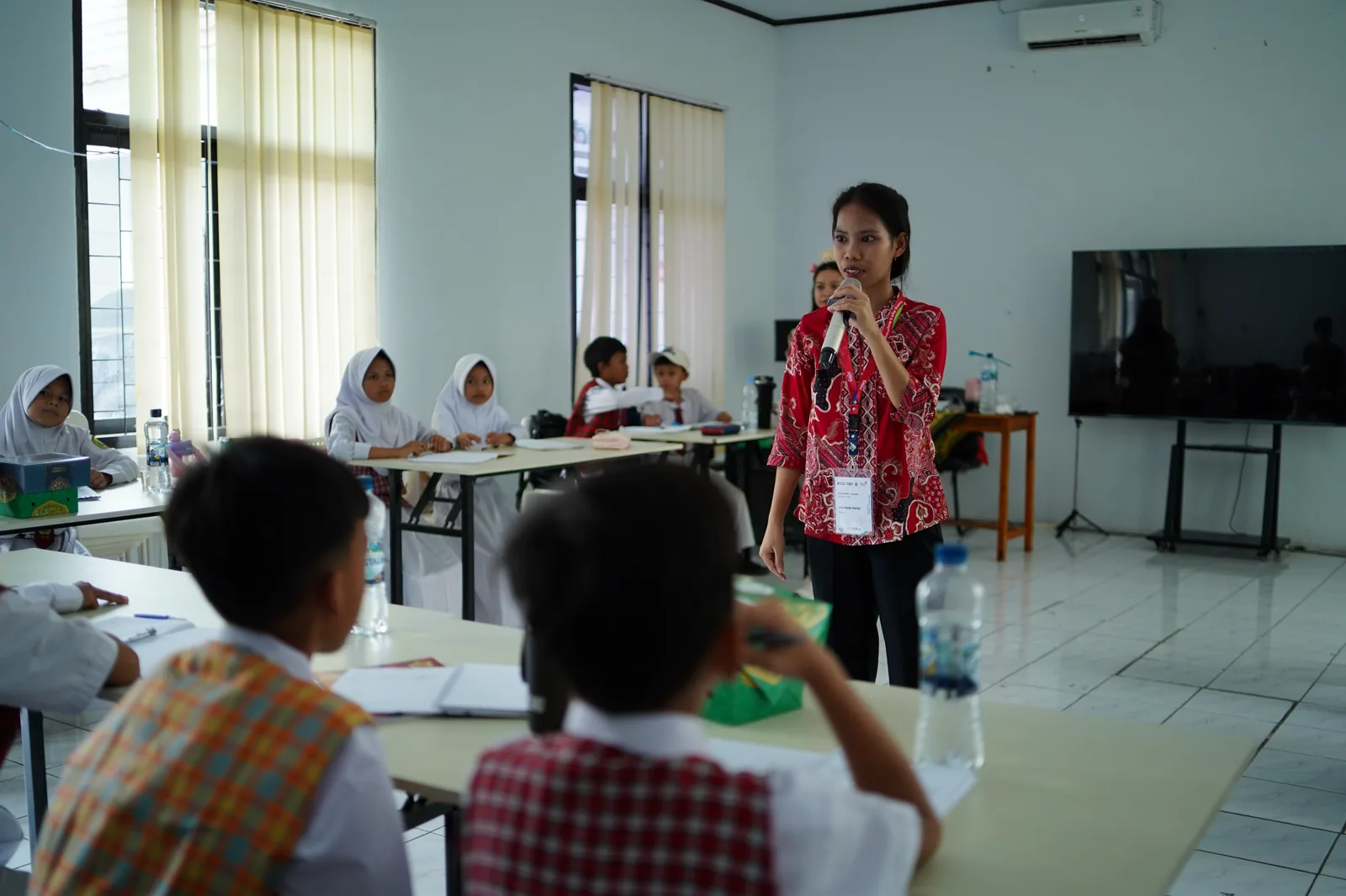 Fasilitator berbicara dengan mikrofon di depan siswa yang duduk berkelompok
